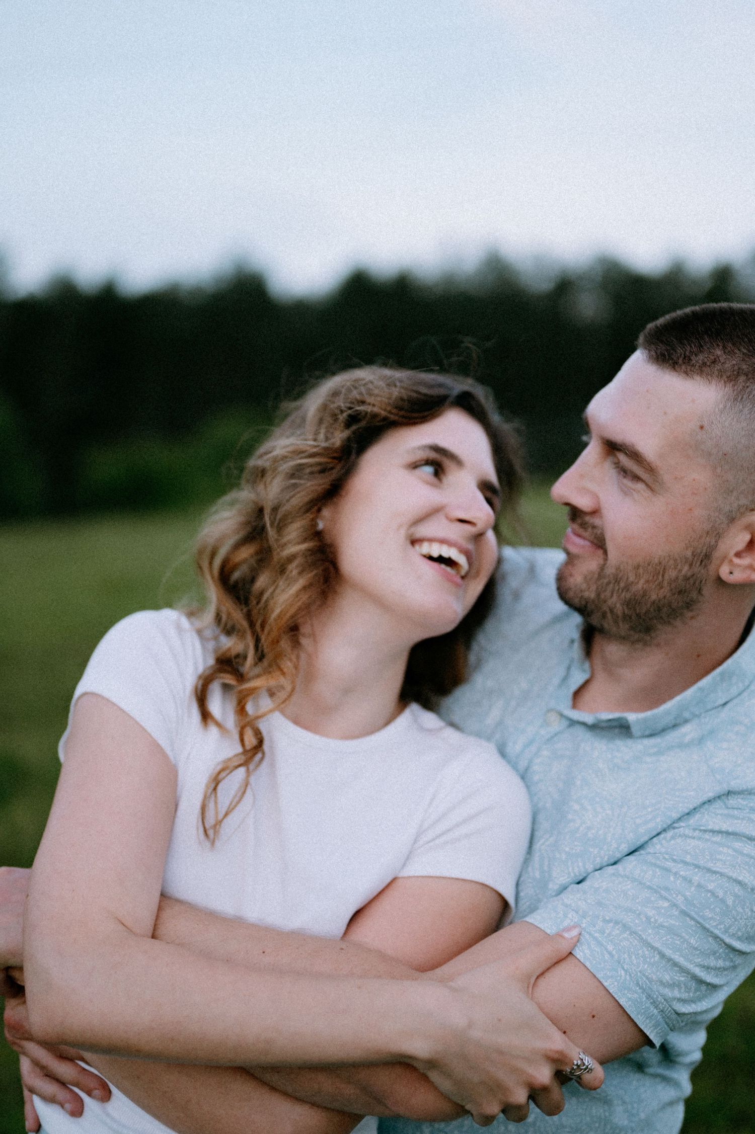 A joyful couple shares laughter while embracing in a field during sunset.