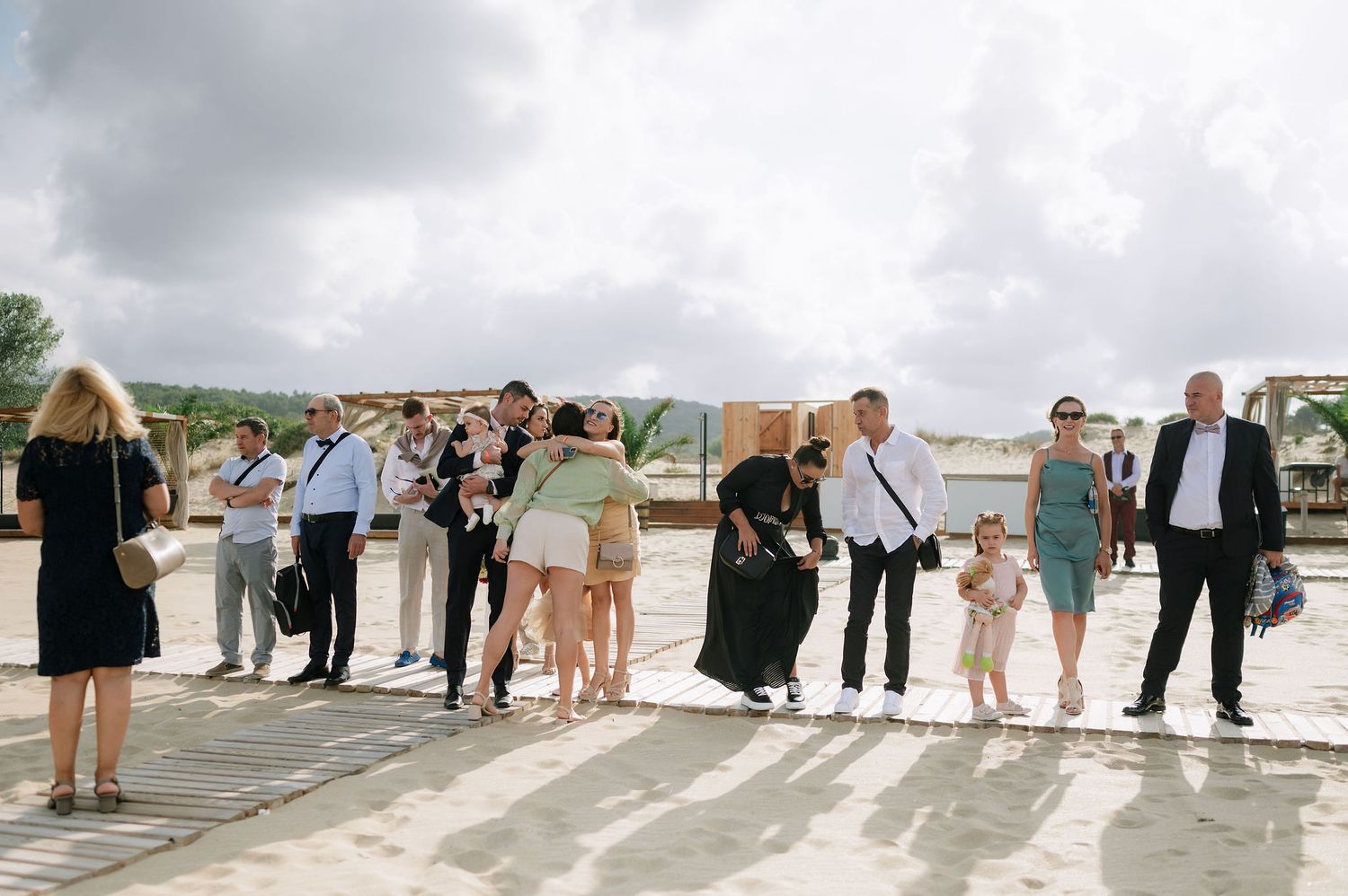 Wedding guests mingle on a beachfront terrace during a daytime celebration.