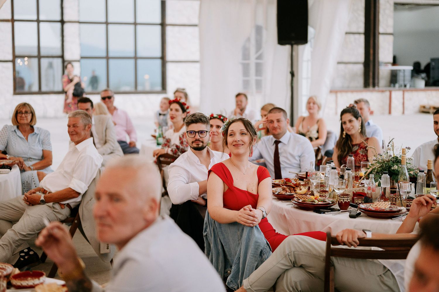 Wedding reception guests seated at decorated tables raise their glasses during speeches.