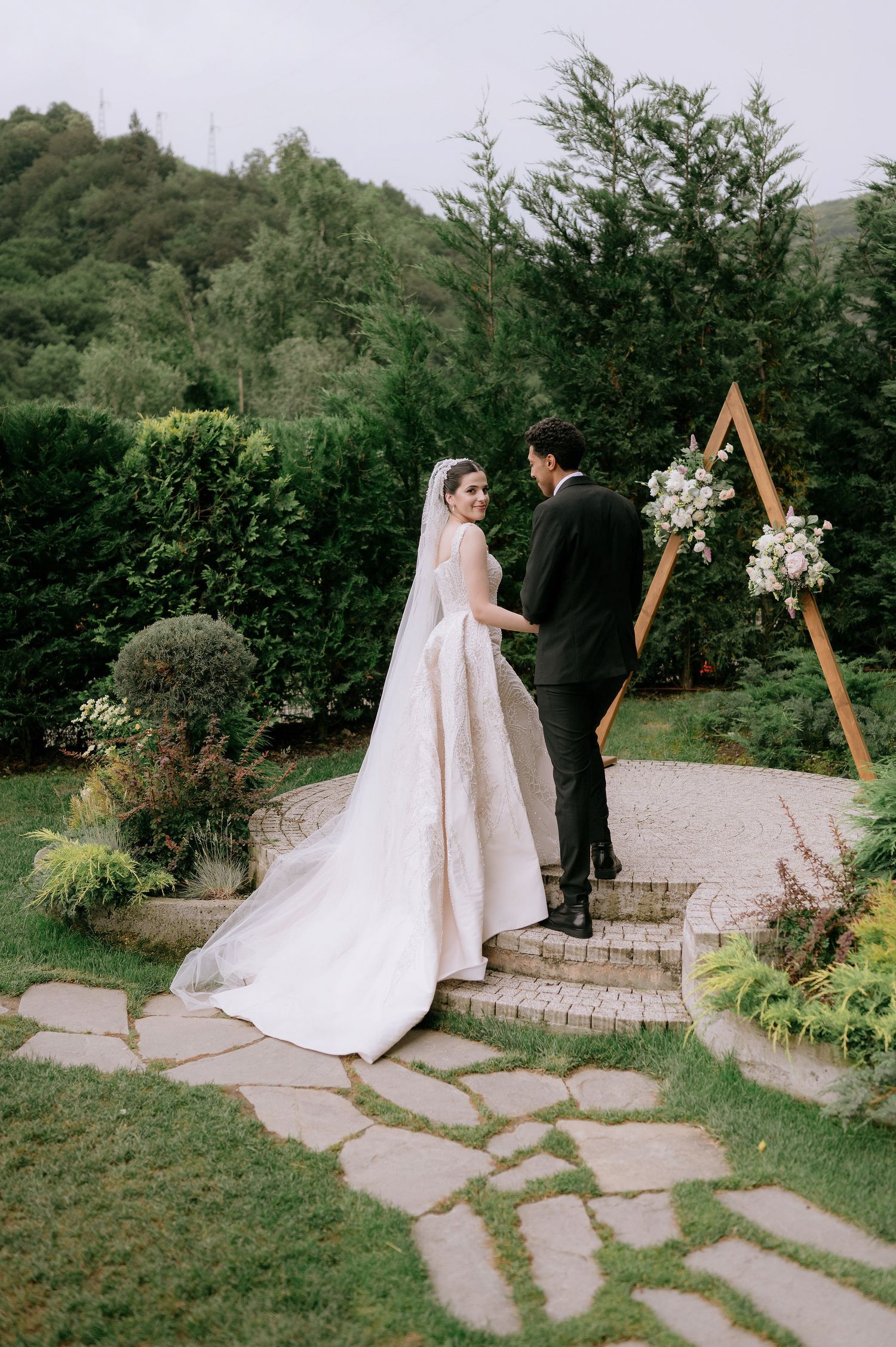 Wedding ceremony site features stone pathway and wooden hexagonal arch surrounded by greenery.