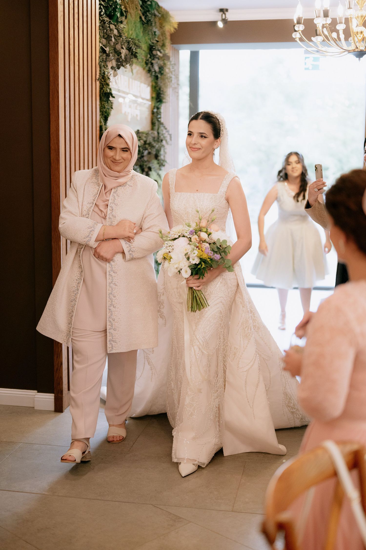 Wedding party members in cream and white formal attire gather in an elegant venue.