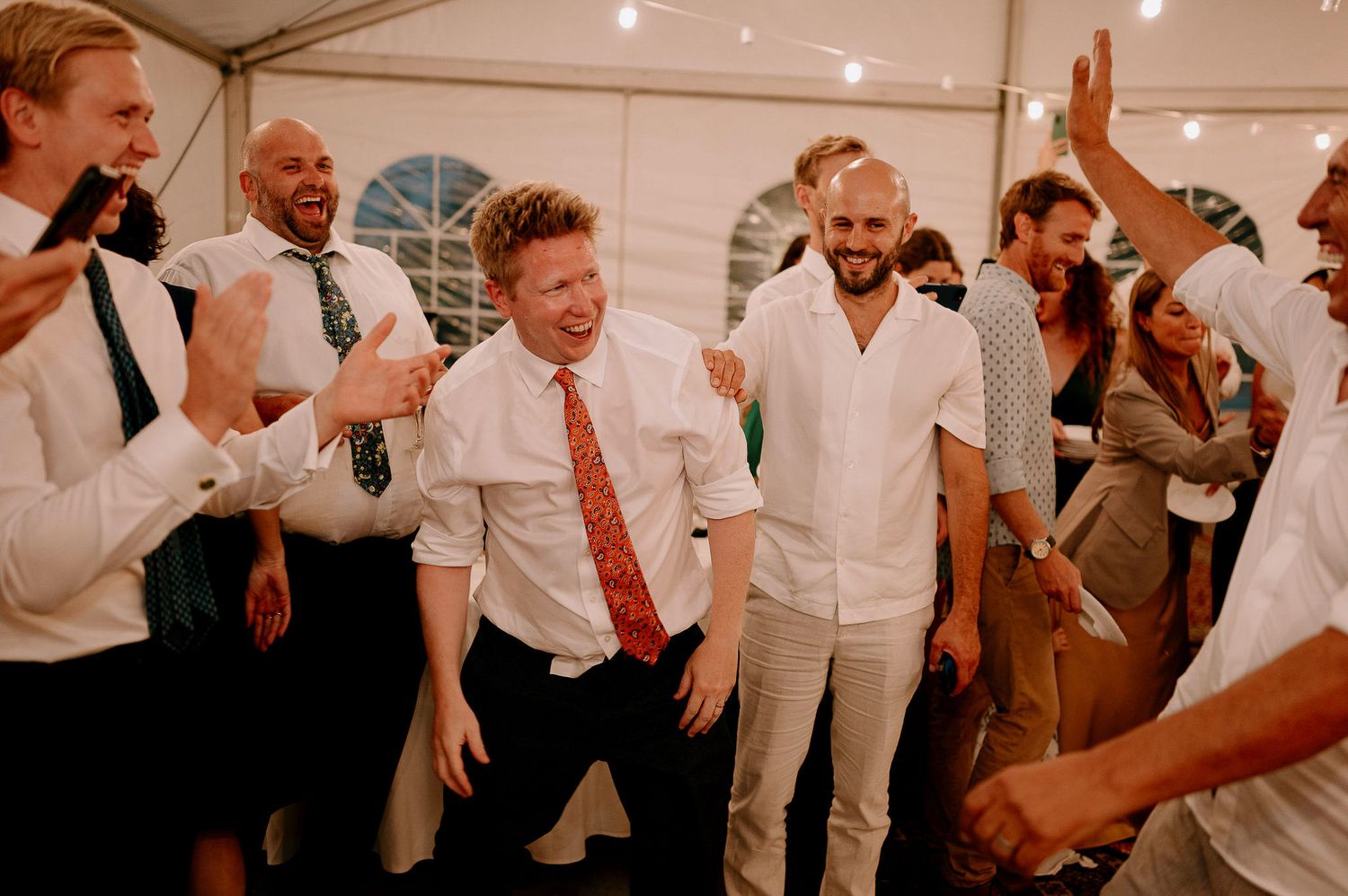 Joyful celebration with guests dancing and laughing under white tent lighting.