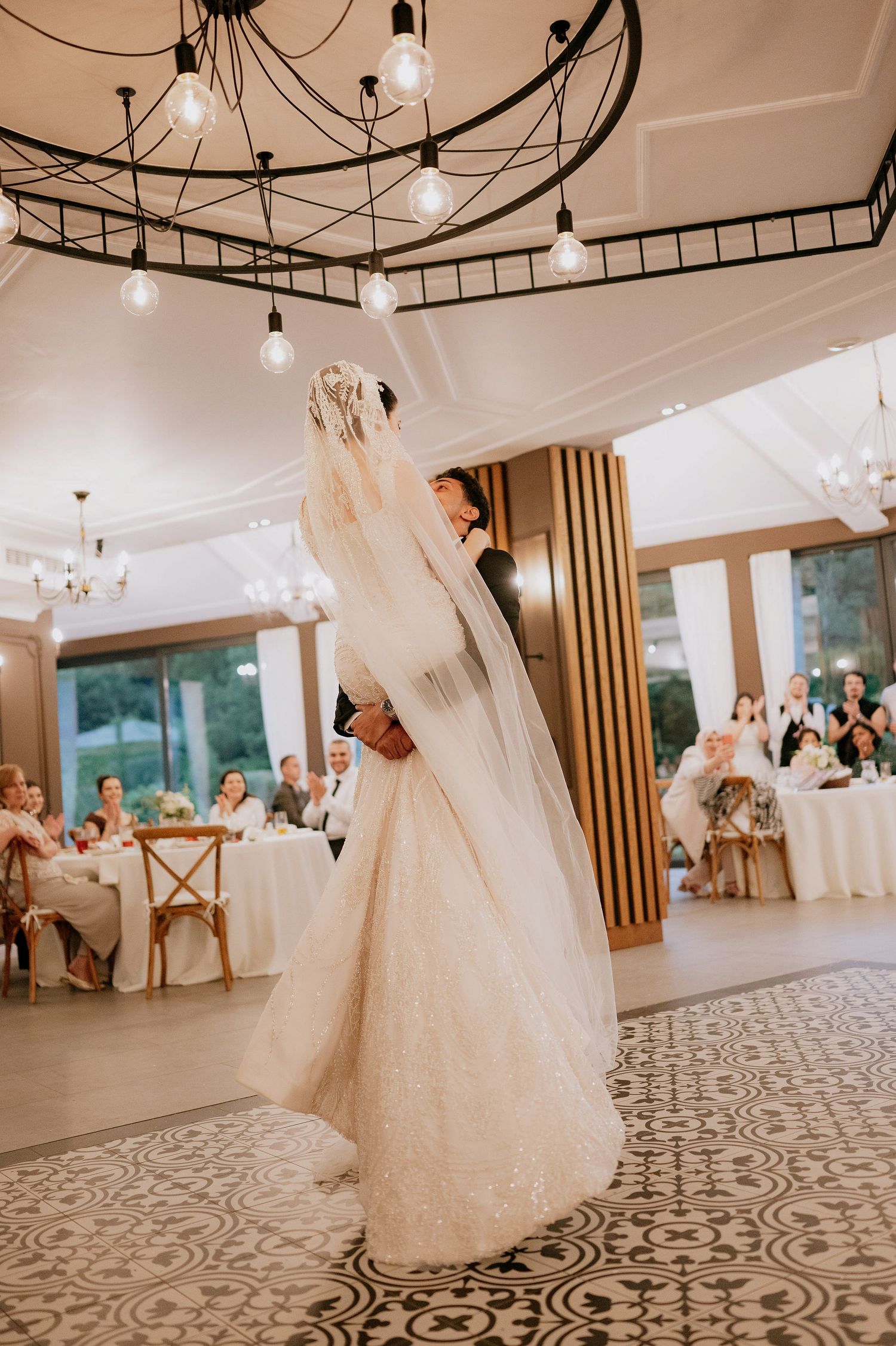 Elegant wedding reception venue with chandeliers and patterned floor features couples dancing in formal attire.