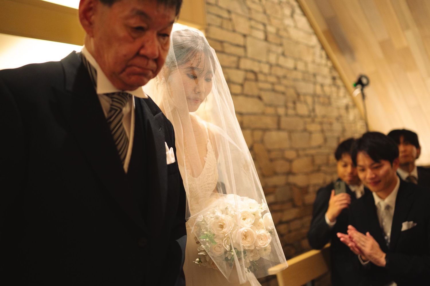 Wedding ceremony taking place in an elegant chapel with stone wall backdrop.