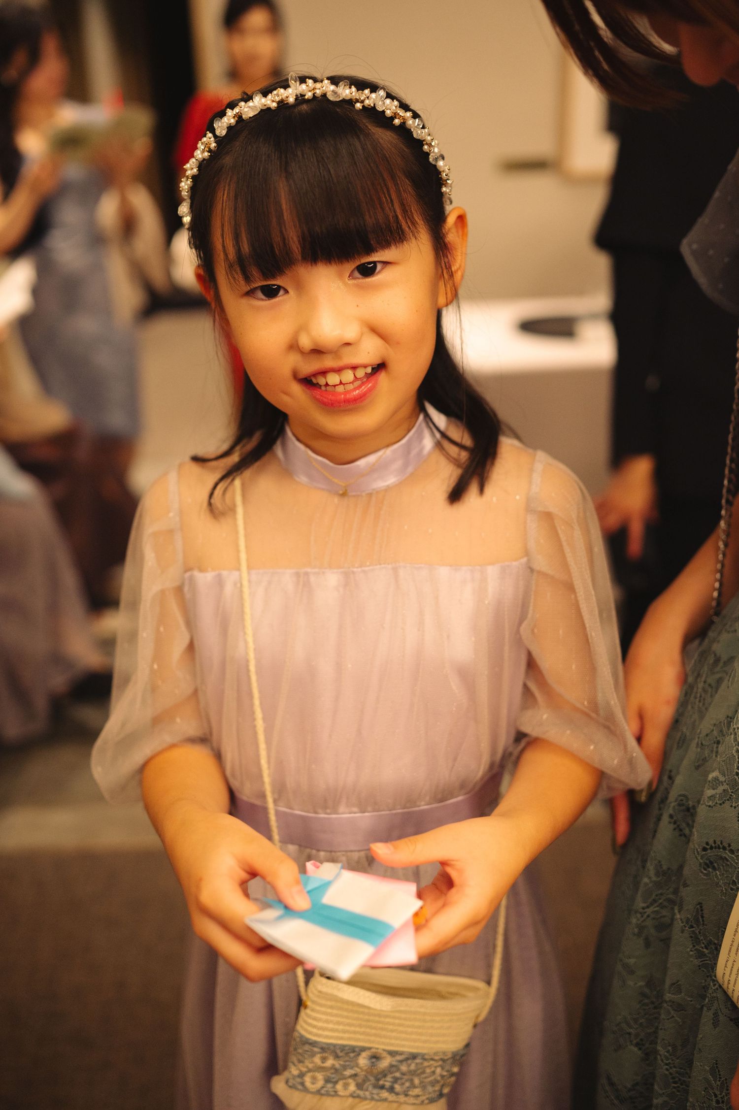 Young attendee in a lavender dress smiling while holding paper cards at an event.
