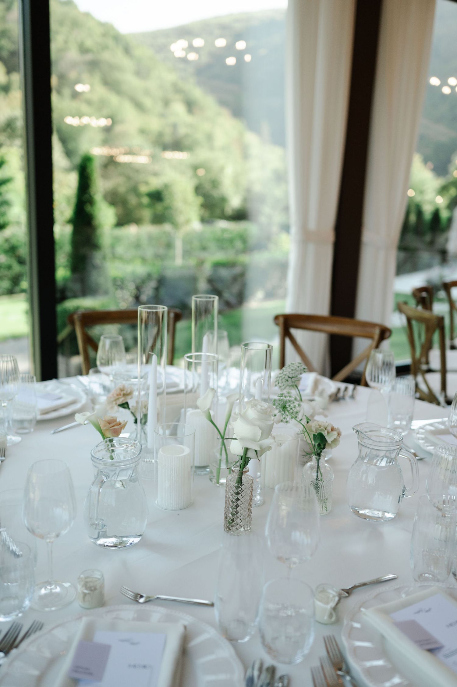 Elegant white table settings at a formal dining event with wine glasses and natural lighting through windows.