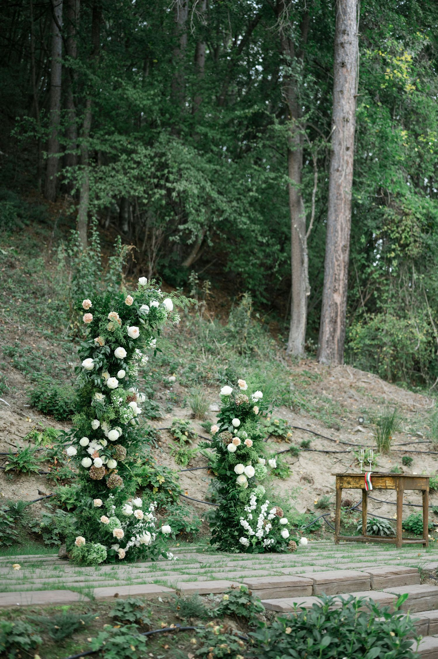 Elegant white roses line a rustic wooden pathway in a wooded garden setting.