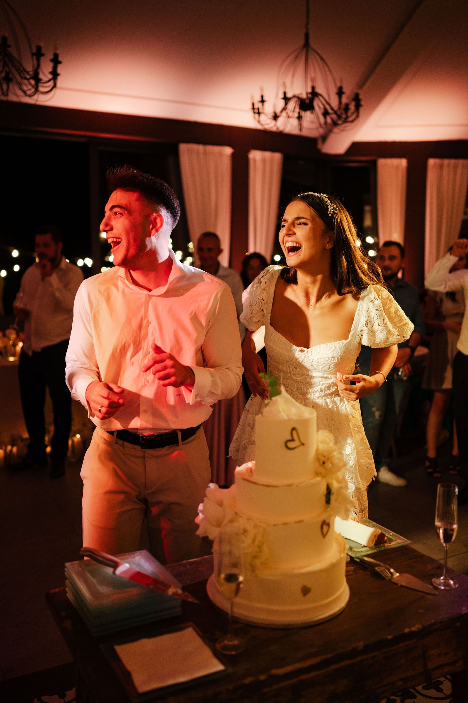 Wedding reception scene with a white cake and joyful celebration in warm lighting.
