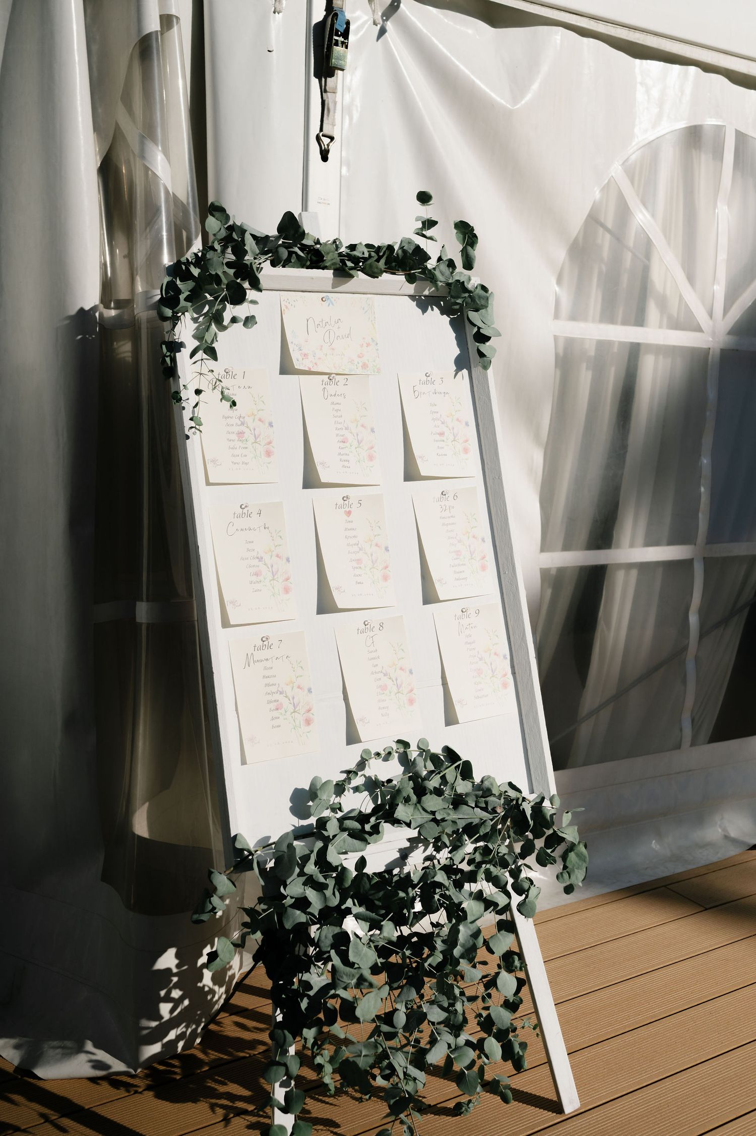 White seating cards displayed against a fabric backdrop with cascading greenery decorations.