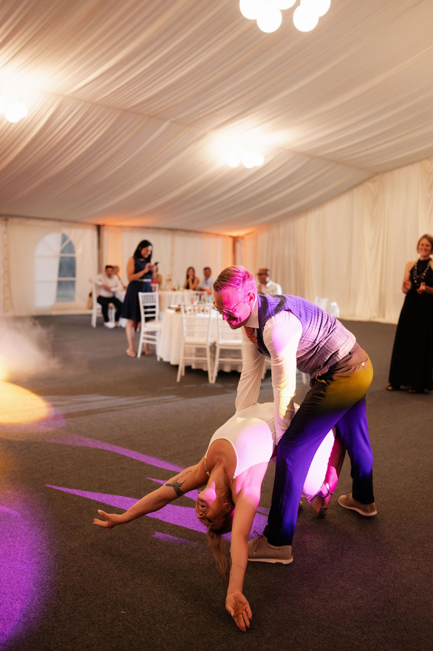People perform a fun dance move while bending down on an illuminated purple dance floor.