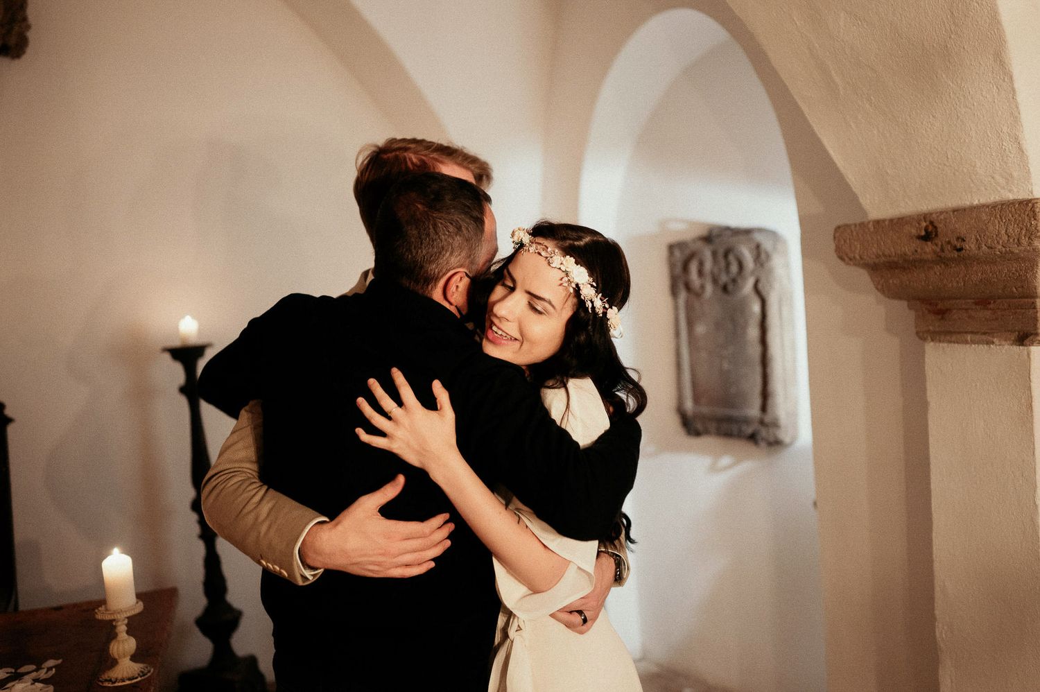 A celebratory embrace captured in warm lighting against white stone walls.
