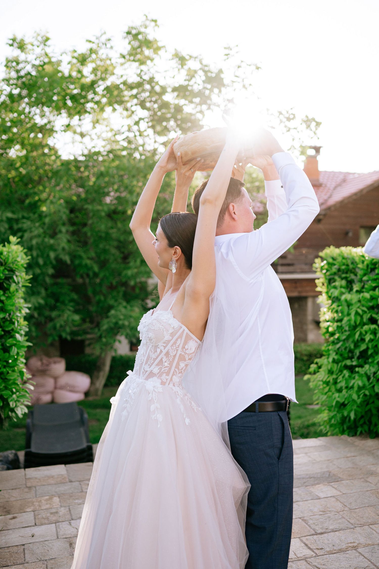 Couple dances joyfully on stone patio during outdoor wedding celebration.