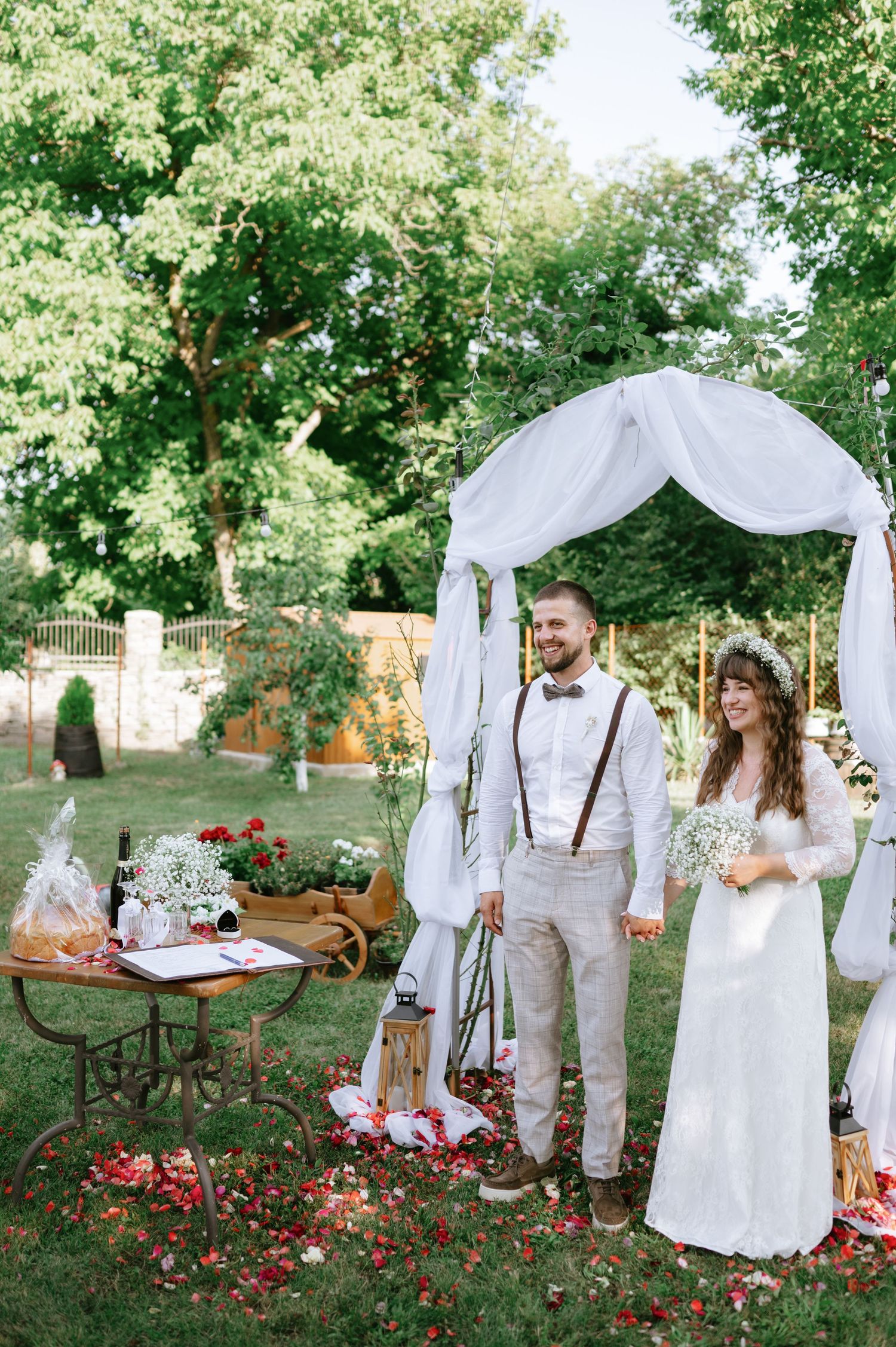 Romantic garden wedding venue with white fabric arch and vintage decor among trees.