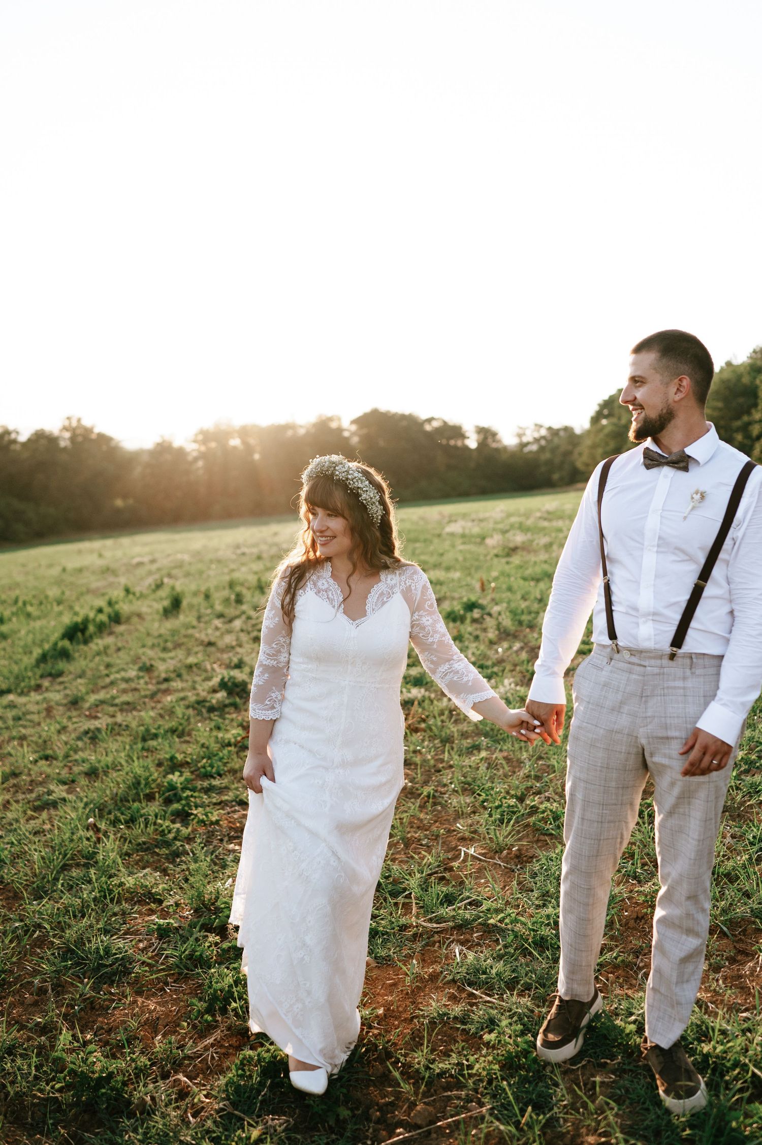 Romantic sunset wedding photo of couple walking through a grassy field.