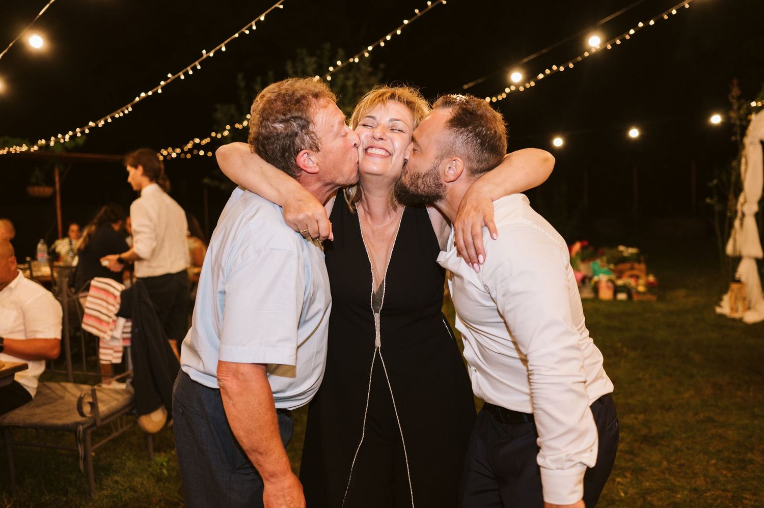 Friends embrace and laugh together under twinkling outdoor party lights.