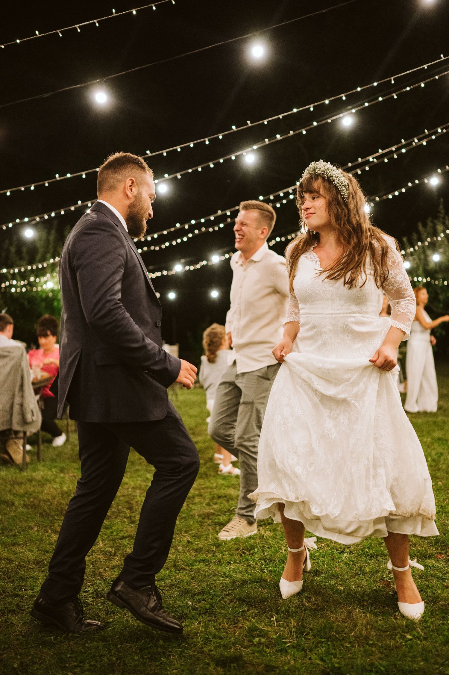Lively dance party at an outdoor wedding reception under twinkling lights.