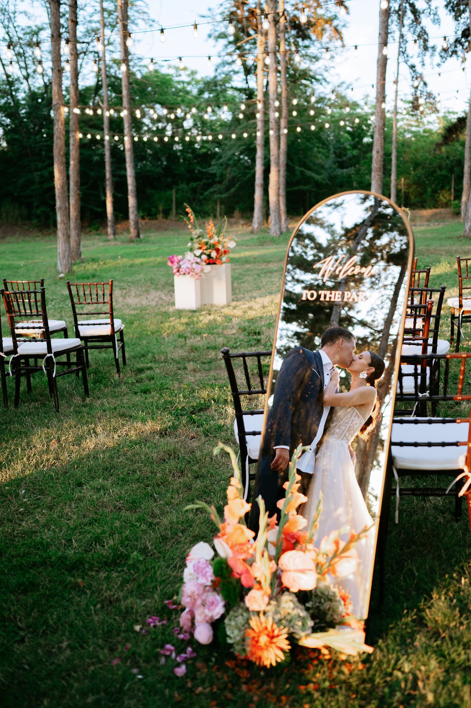Pine forest wedding venue with wooden chairs and hanging lights creating magical atmosphere.
