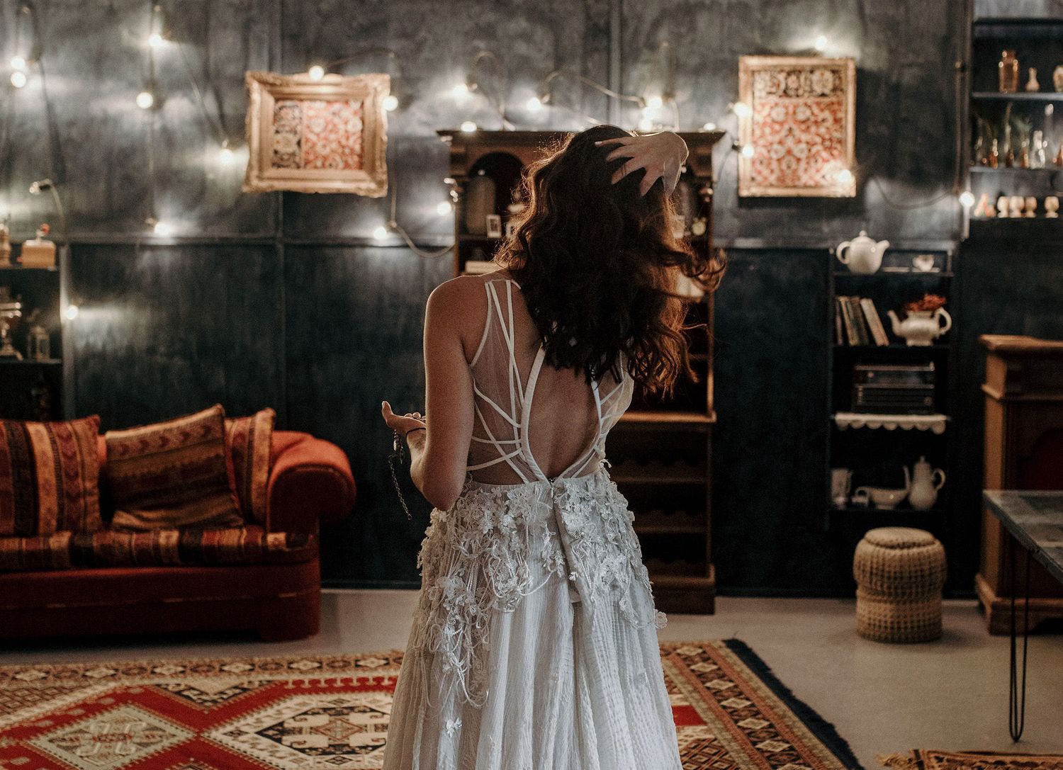 Back view of an elegant white lace wedding dress in a moody vintage-style room with hanging lights.