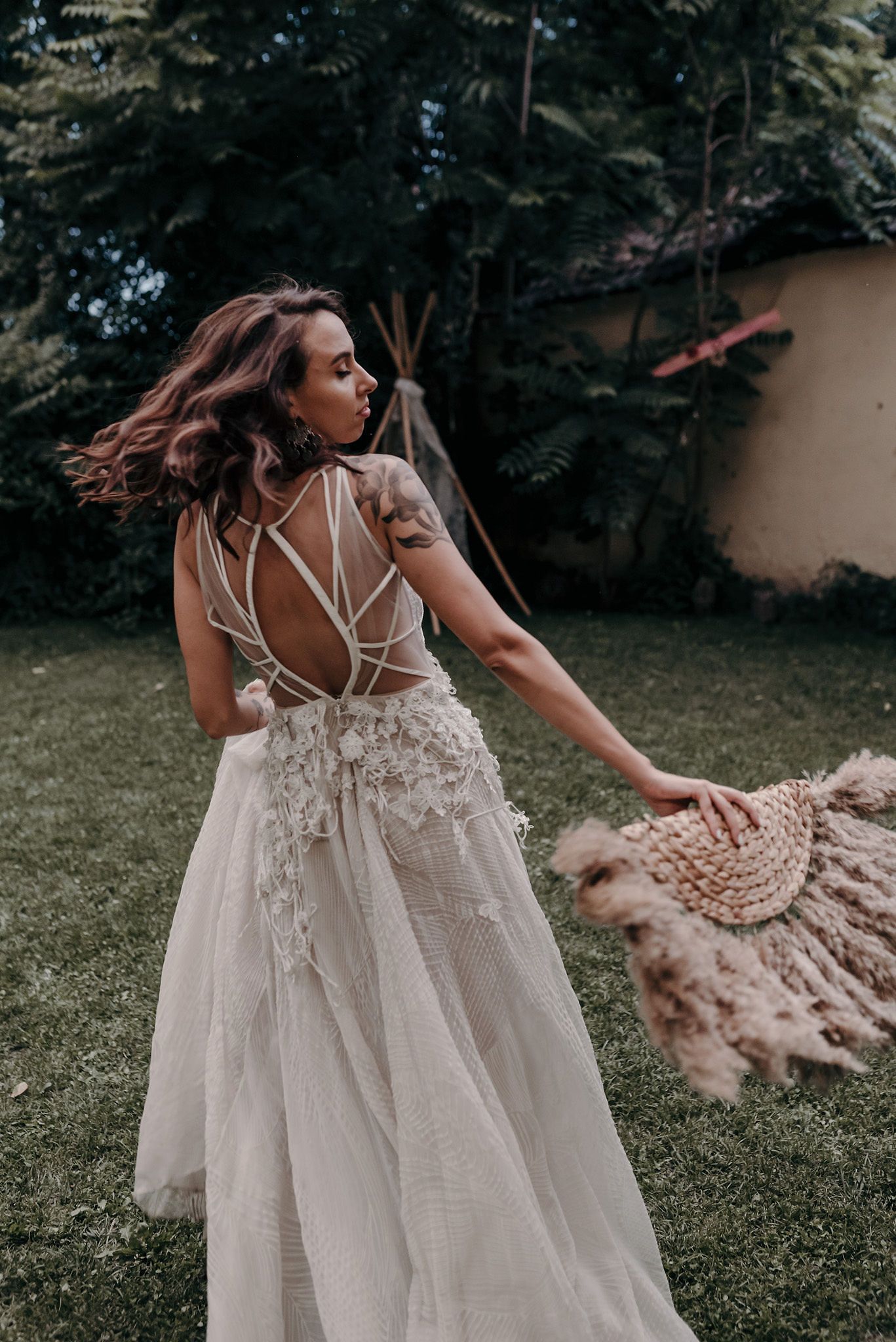 A romantic bohemian wedding dress with intricate strappy back detail and flowing tulle skirt captured in an outdoor garden setting.