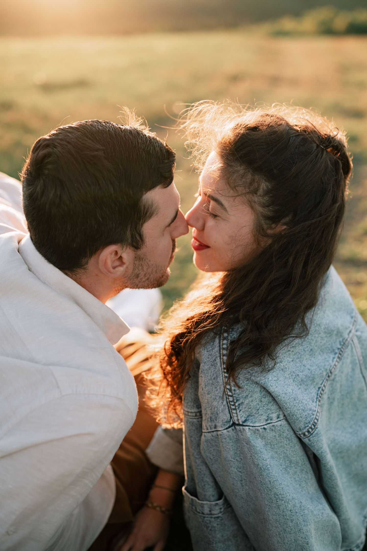 Romantic couple sharing tender kisses in golden sunlight while wearing denim and white clothing.