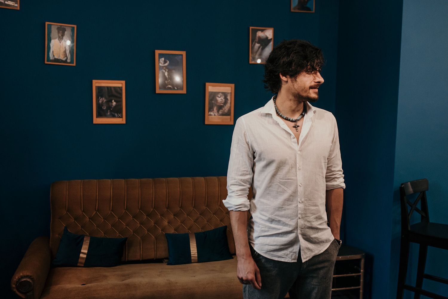 Person in white button-down shirt standing against deep blue wall with framed photos.