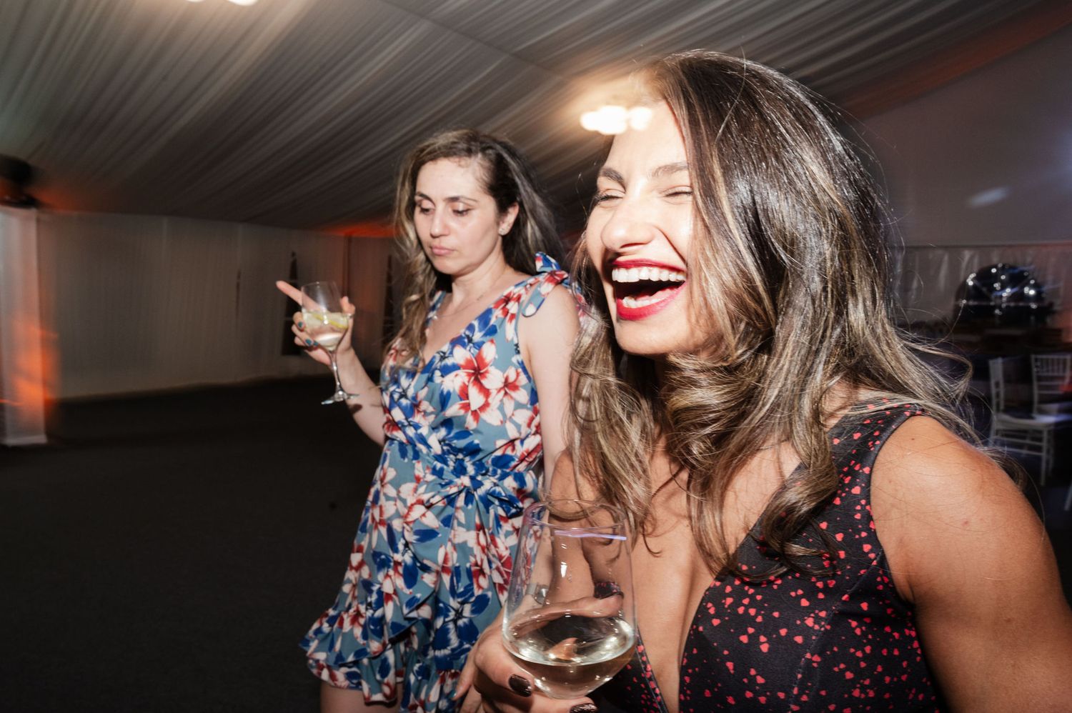 People dancing and celebrating at a party with drinks and colorful outfits in a dimly lit room.