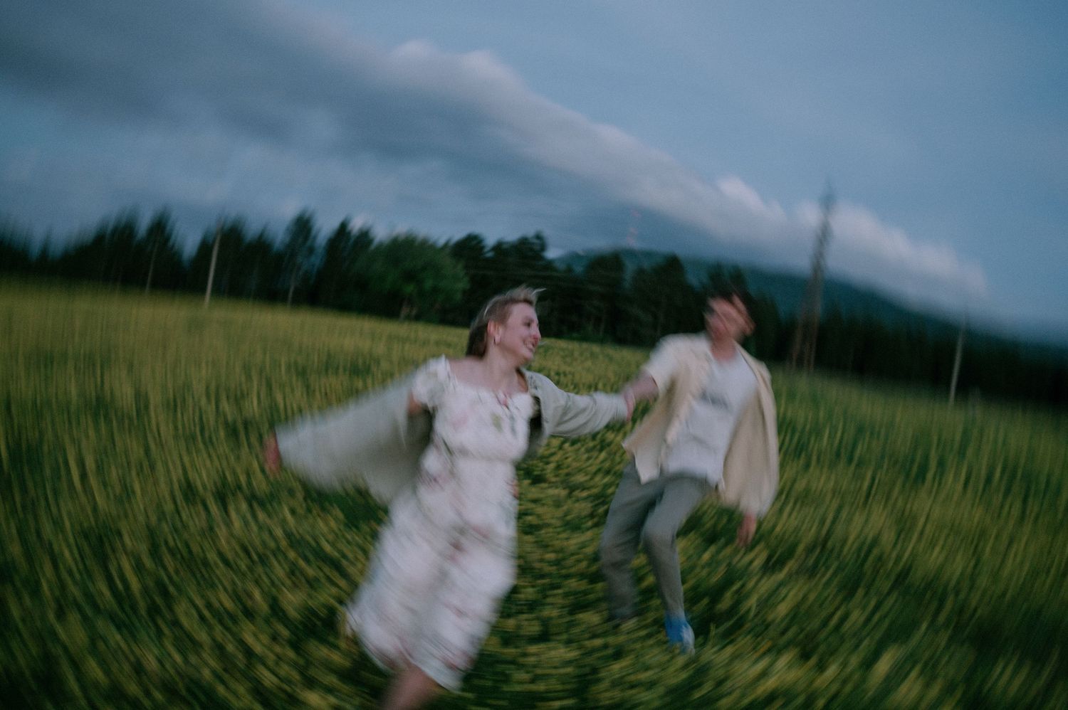 Playful couple runs through a flowering meadow during golden hour.