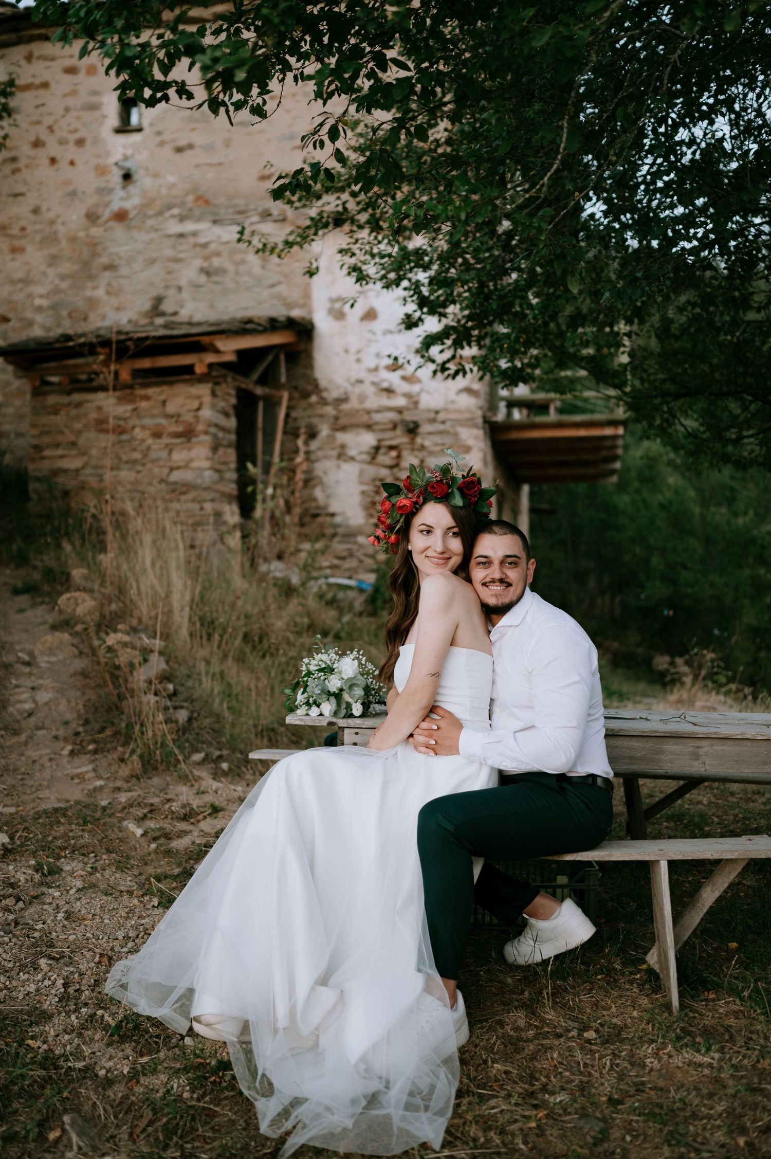 Newlyweds share intimate moment on wooden bench during outdoor photoshoot.