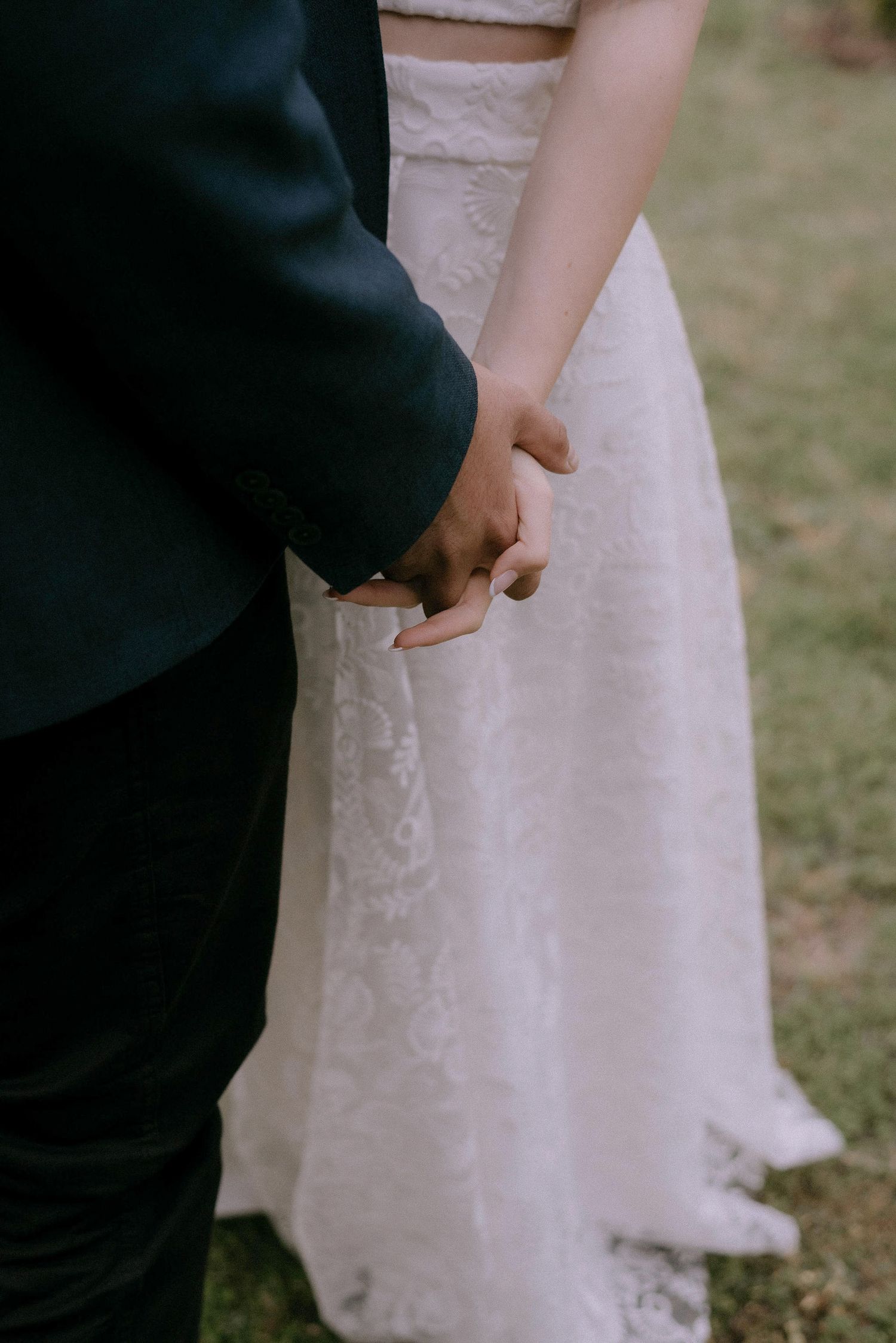 Detail shot of hands against a white lace wedding dress.
