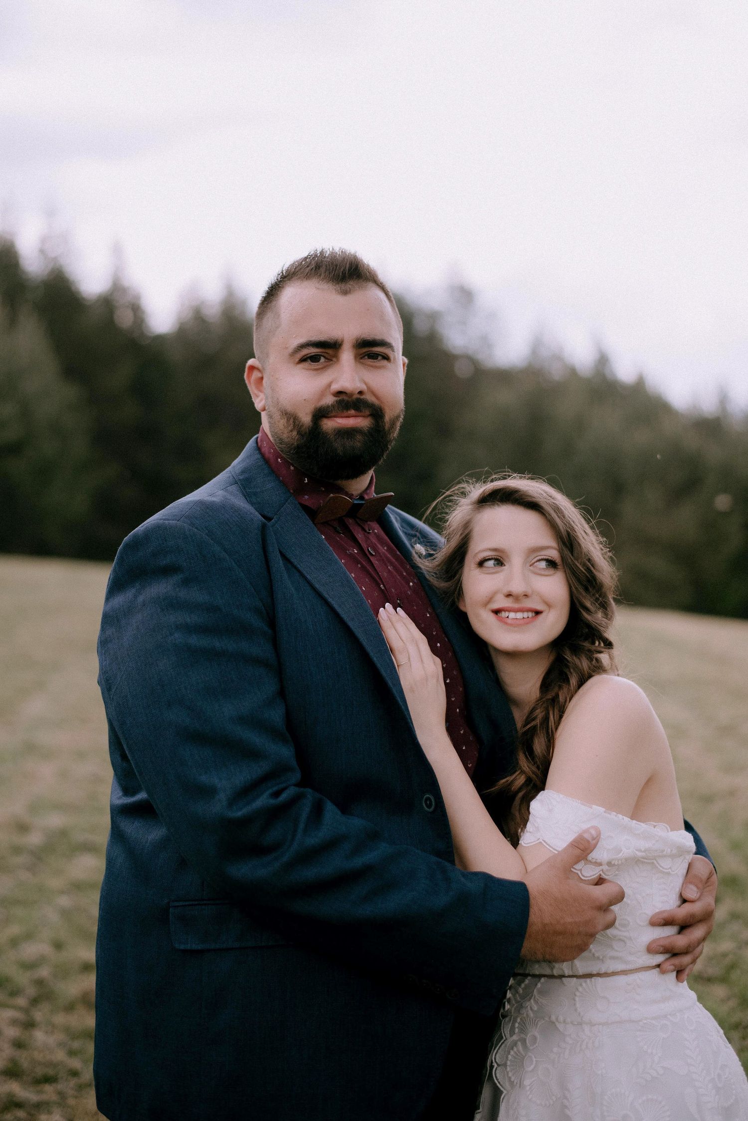 A tender embrace between newlyweds on a scenic hillside with forest backdrop.