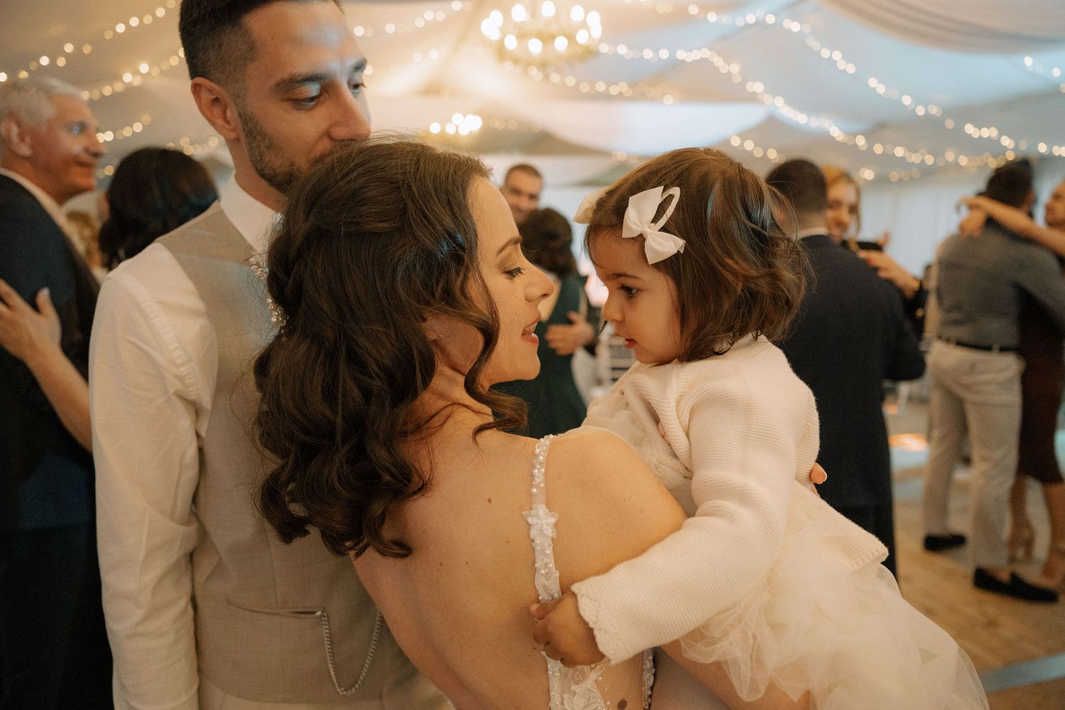Bride and groom sharing a tender moment with a young flower girl in white at a romantic wedding reception.