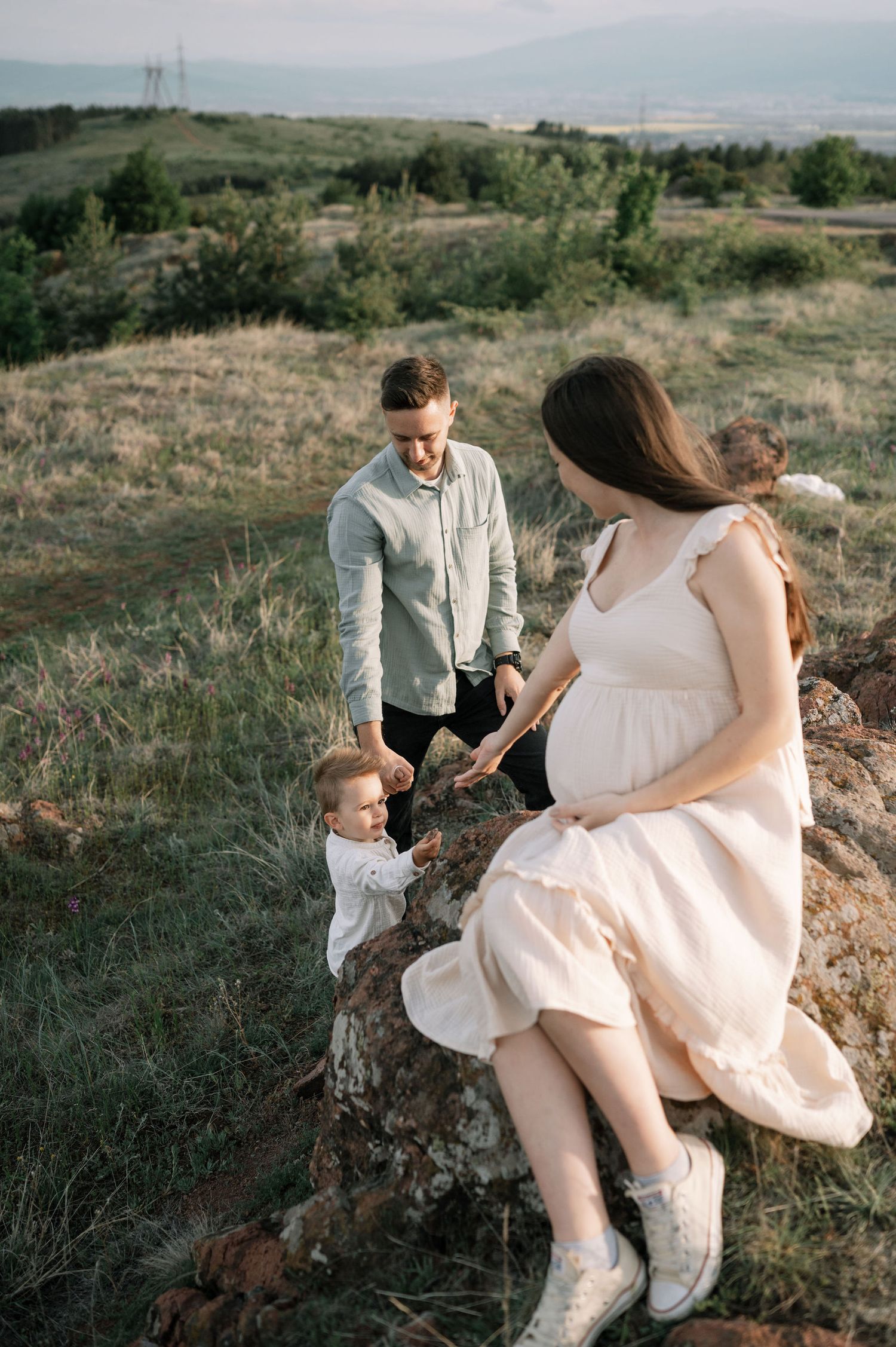 A family enjoys a tender moment together on a grassy hillside during a sunset photoshoot in nature.