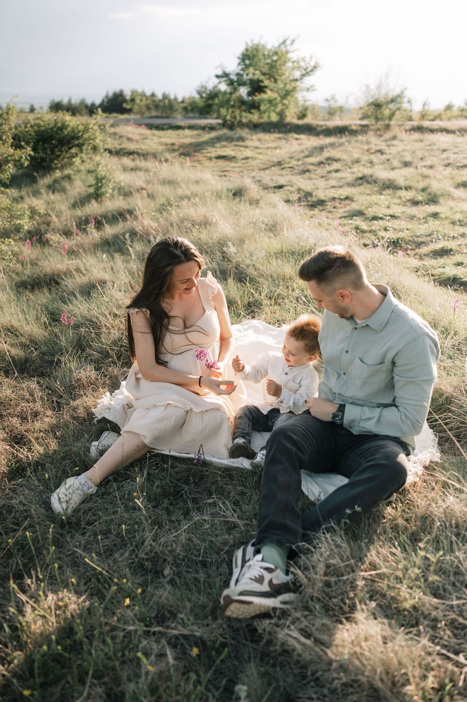 A couple lounges together in a grassy field on a sunny afternoon, sharing intimate moments in nature.