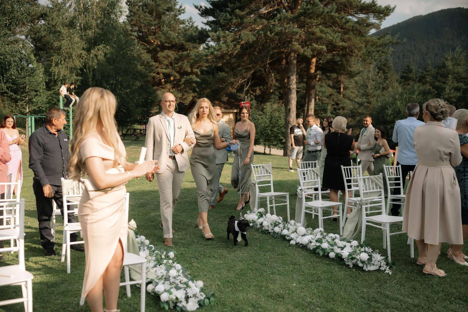 Outdoor wedding ceremony setup with white chairs and floral aisle decorations against a mountain backdrop.