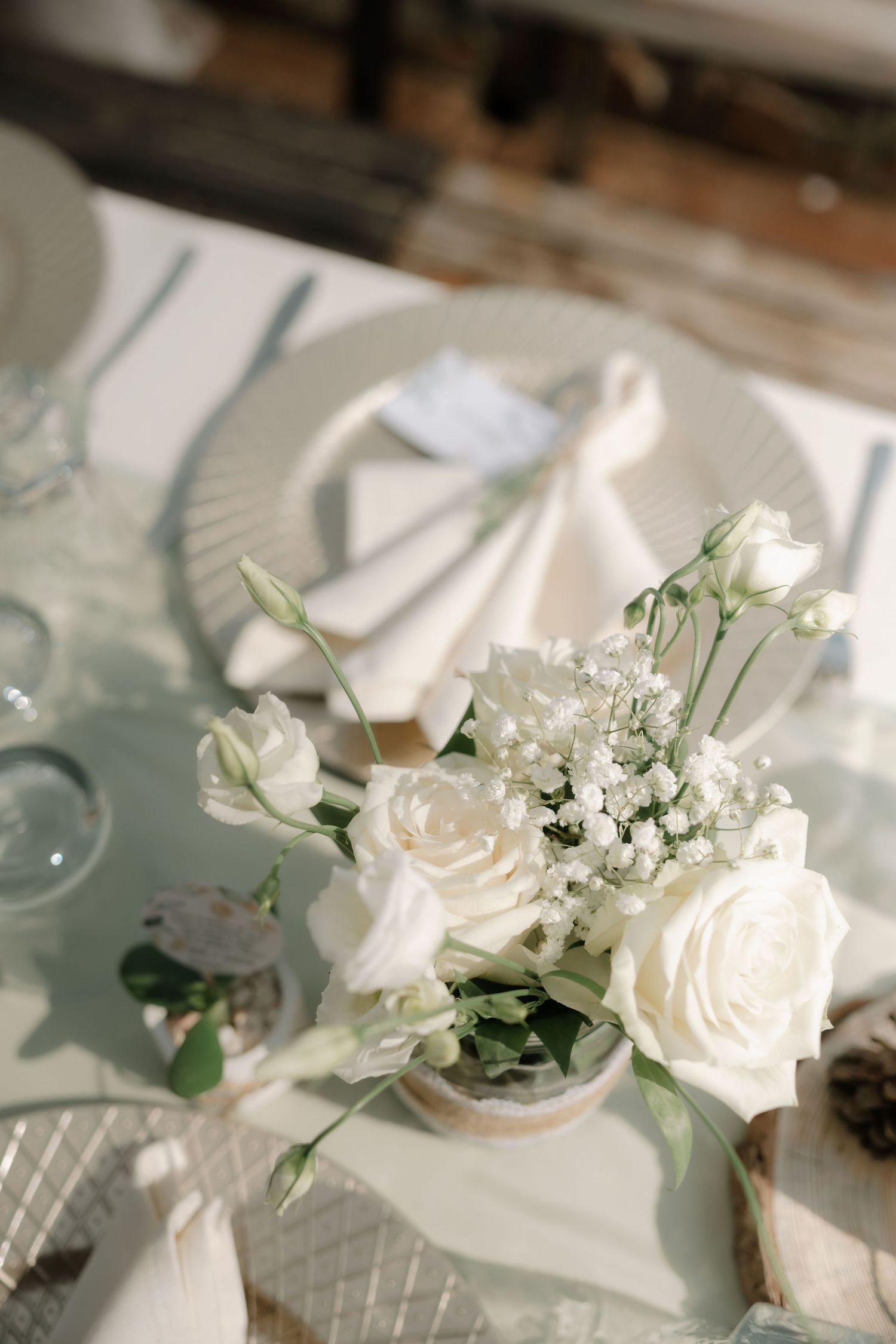 Elegant white roses and baby's breath centerpiece arrangement on a table with white place settings.