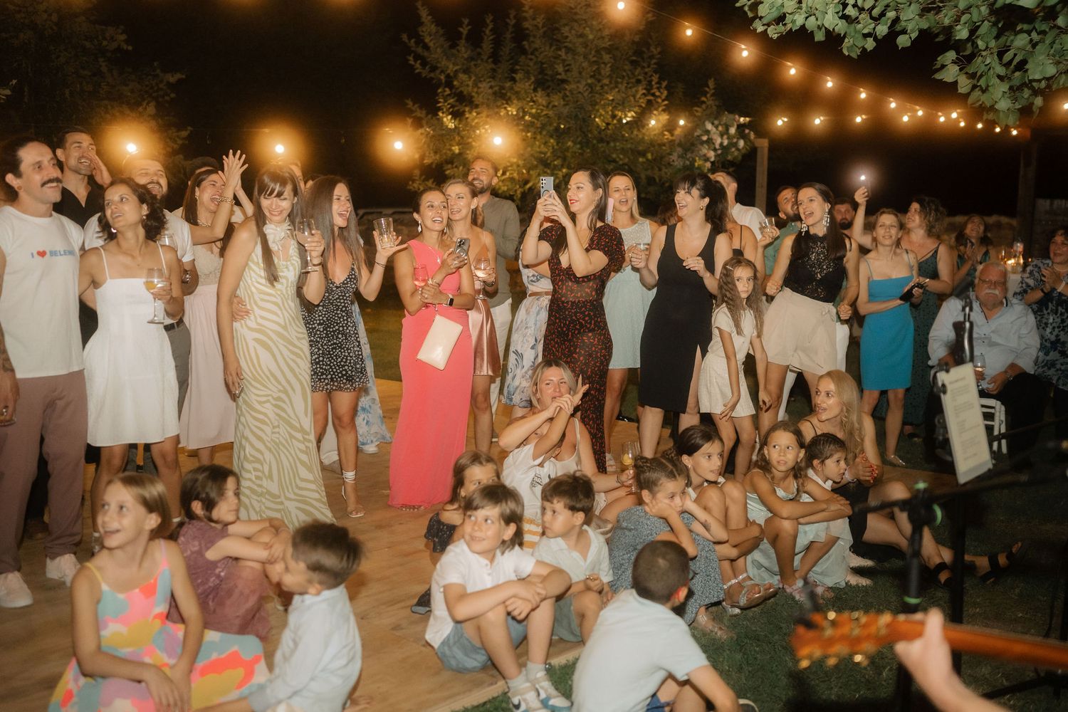 Wedding guests dance and celebrate on an outdoor dance floor illuminated by warm string lights at night.