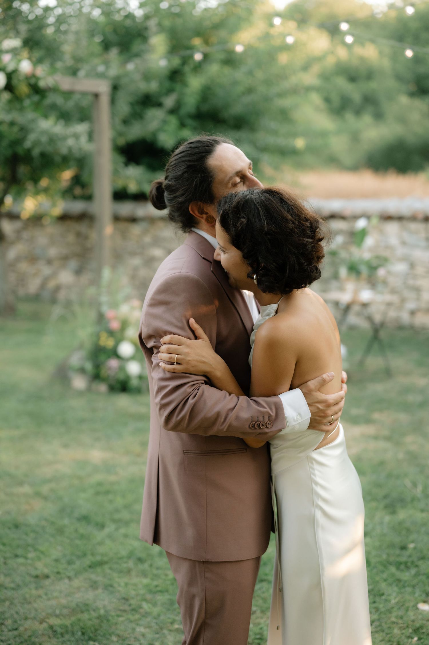A couple embraces in a romantic moment outdoors during golden hour in a garden setting.