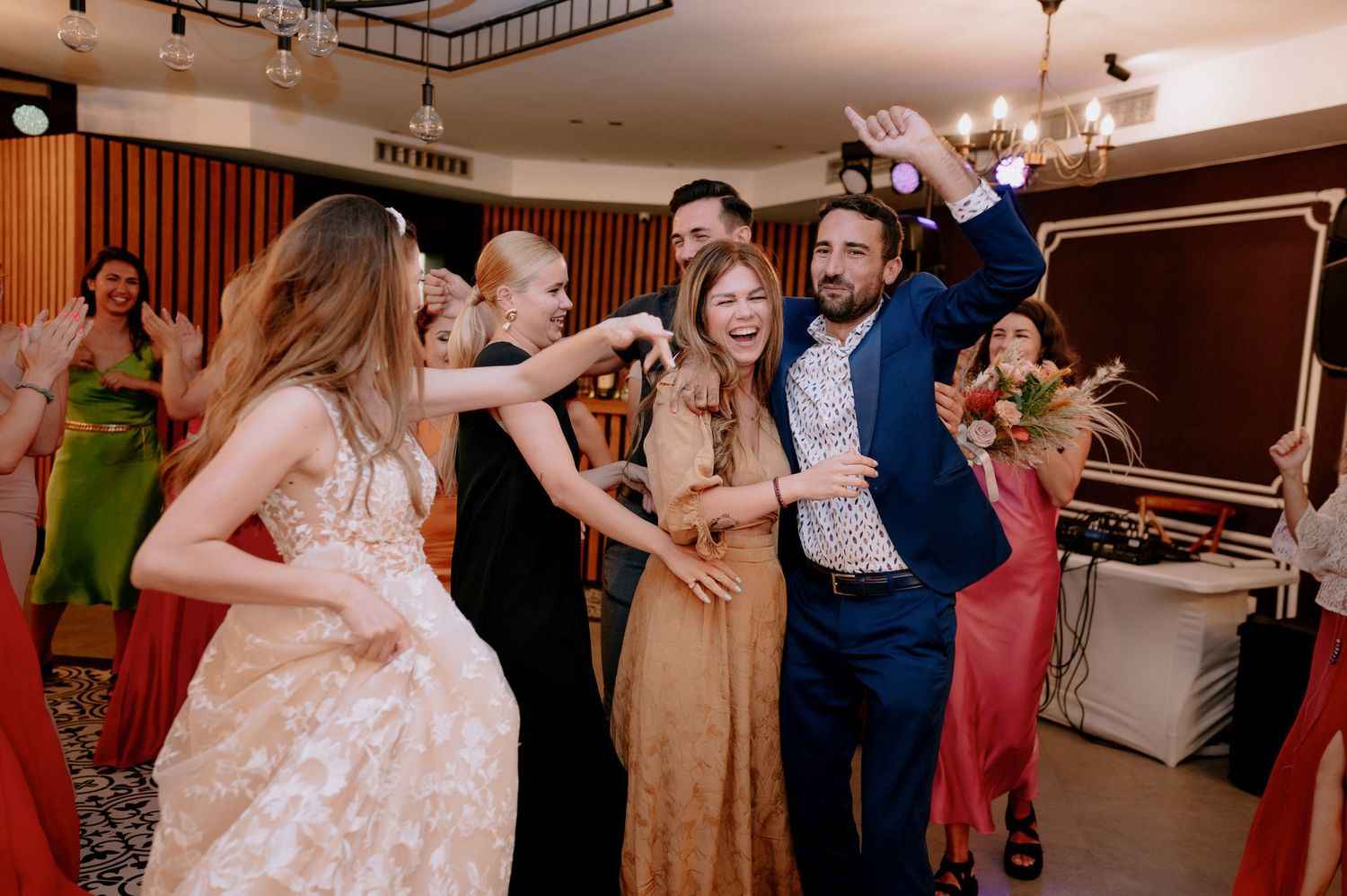 Wedding guests dance and celebrate together on the dance floor at an indoor reception venue.