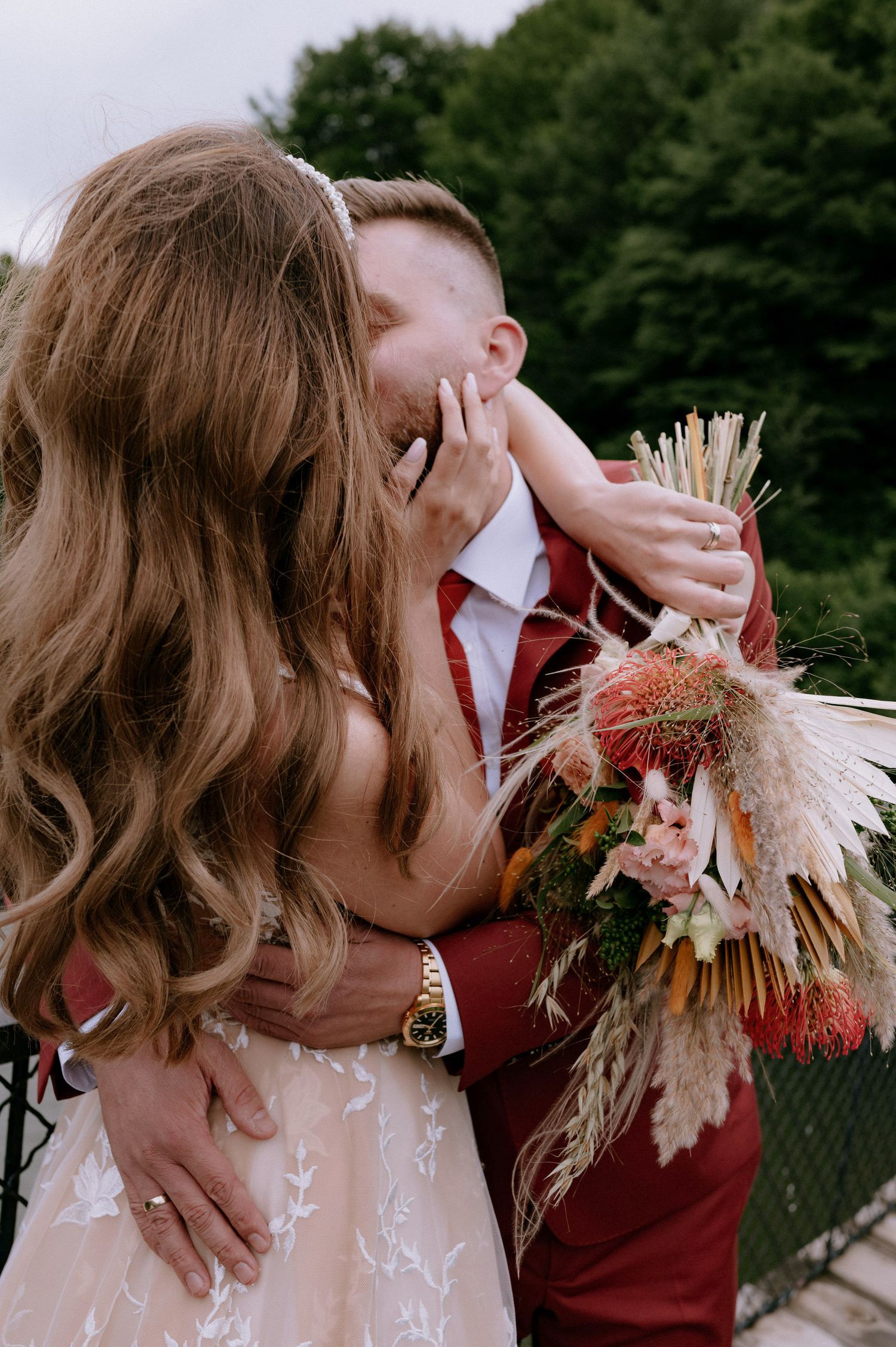 A romantic wedding moment captured outdoors with a burgundy suit and dried floral bouquet featuring pampas grass.