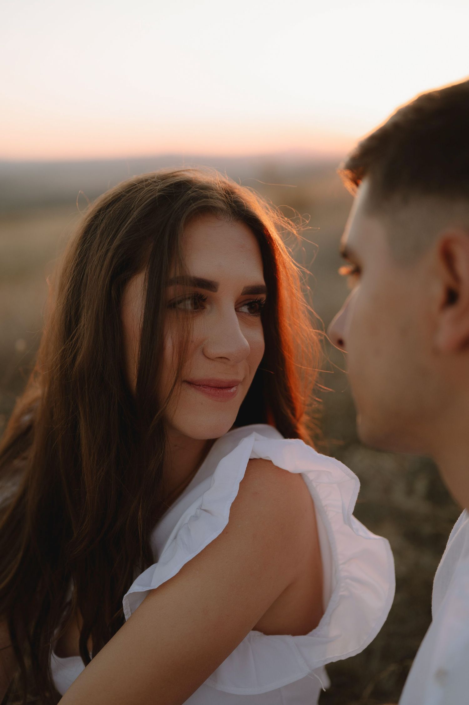A romantic sunset portrait of a couple in white clothing with warm golden light illuminating their faces.