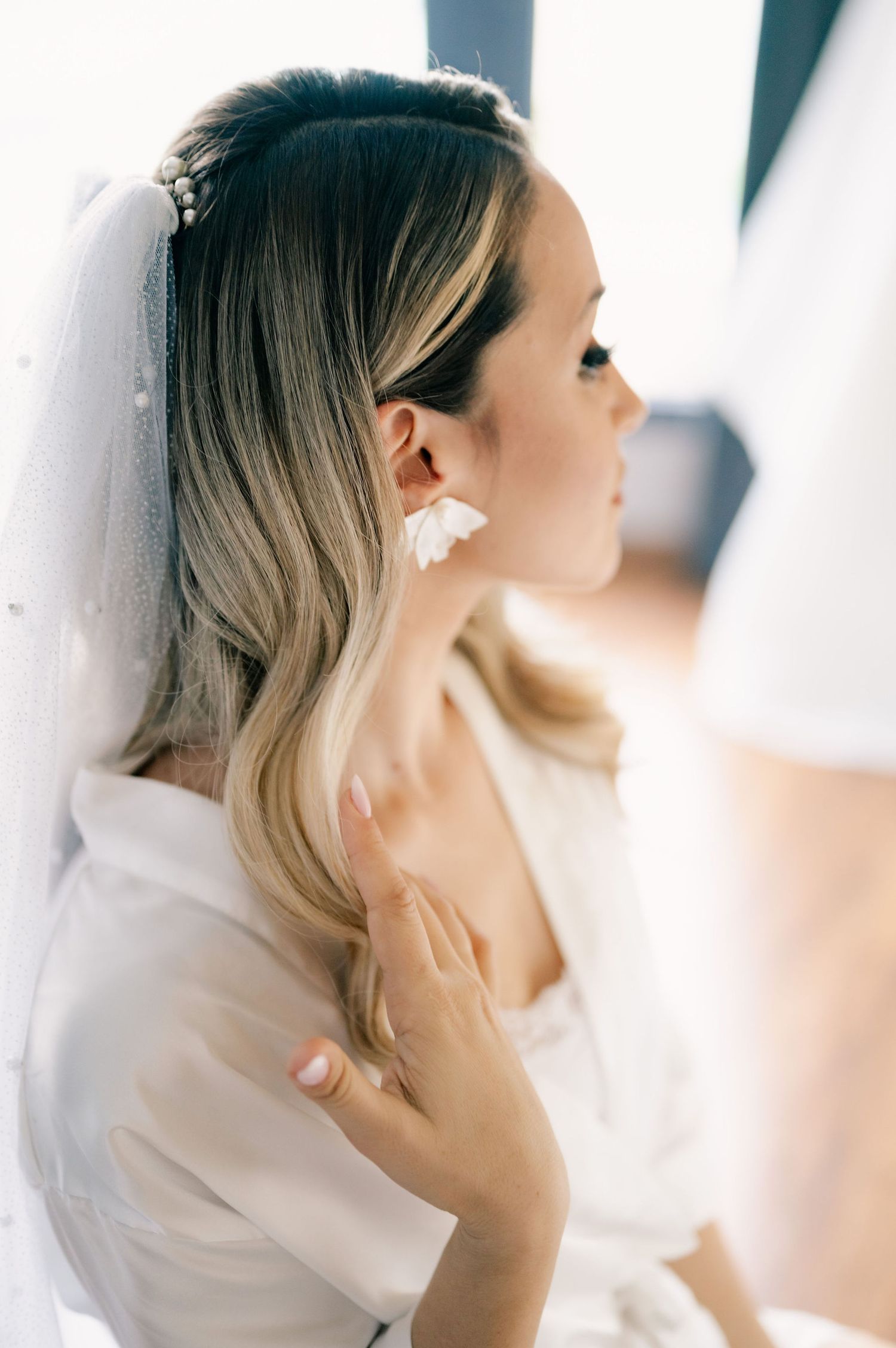 A bride wearing a delicate veil and pearl earrings looks away in a soft, ethereal profile portrait series.