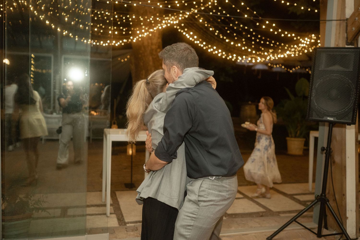 People dance under warm string lights at an evening wedding reception on an outdoor patio.