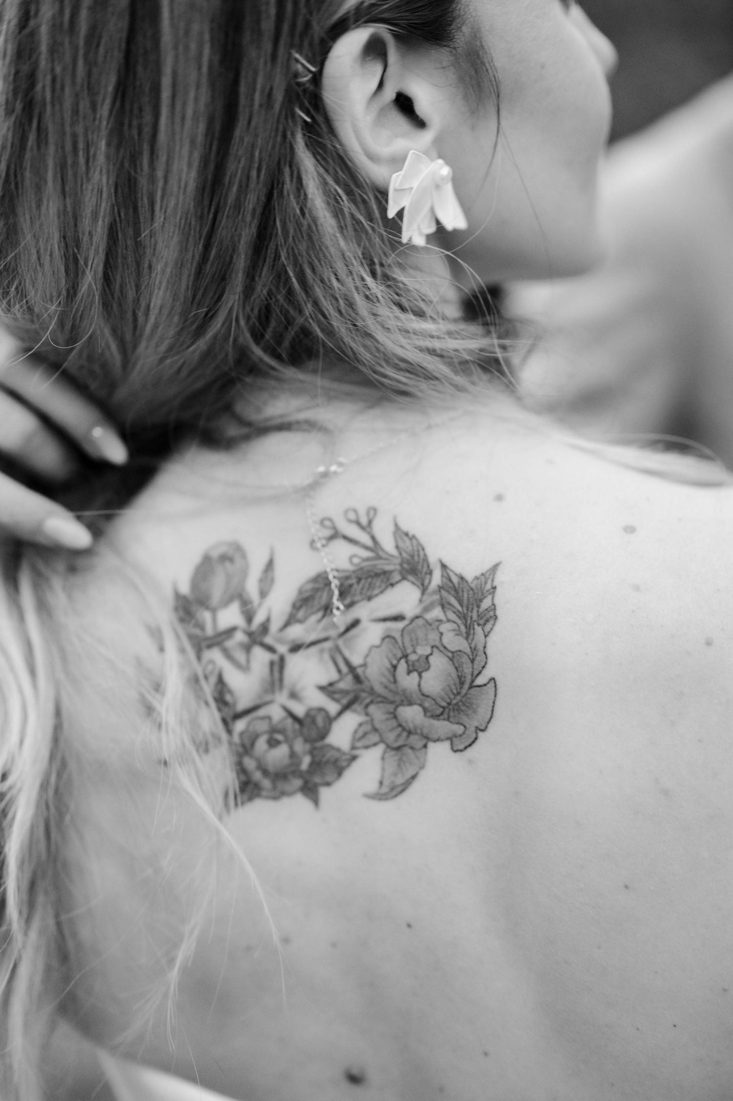 Black and white photo series showing delicate floral tattoo art on a person's upper back and shoulder area.