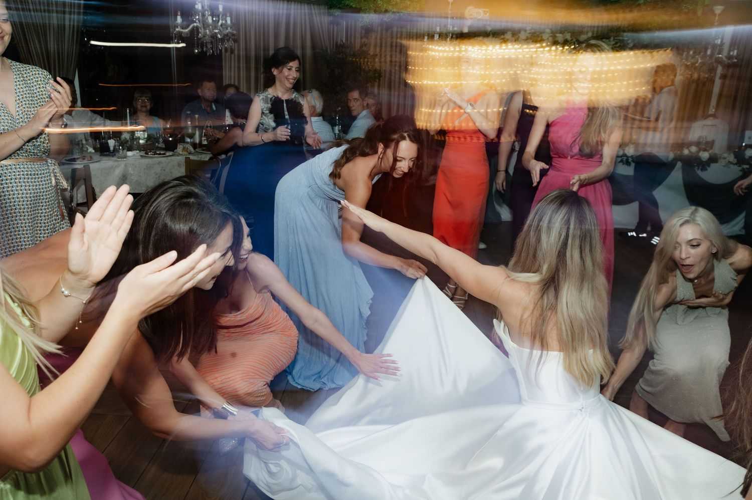 People dancing and celebrating at a lively party with colorful lights and decorations in the background.