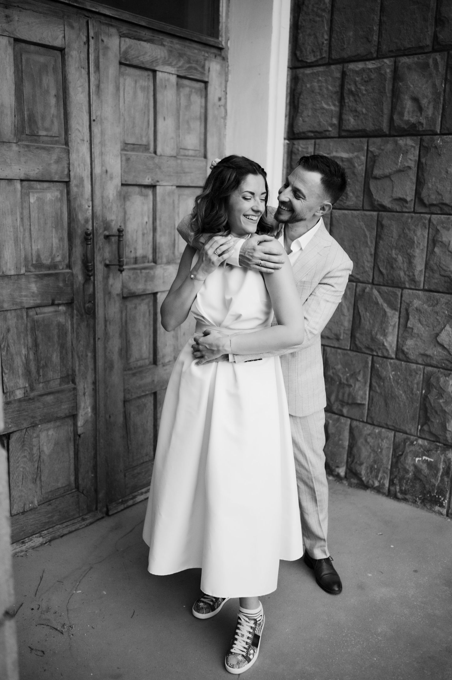 Black and white photo series showing a couple in casual and formal wear embracing against a stone wall backdrop.