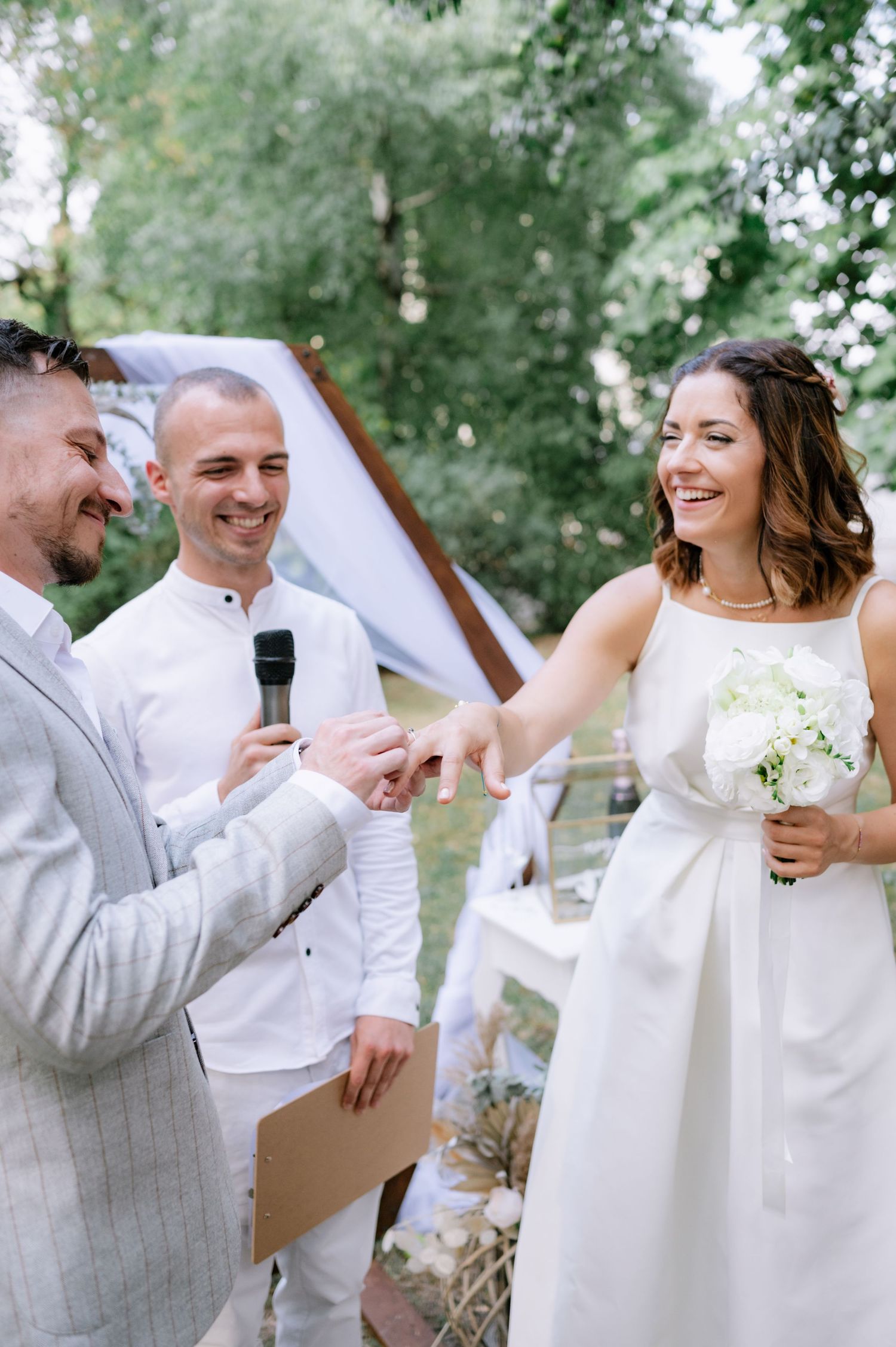 A joyful wedding ceremony moment outdoors with a bride in white dress and two men in light colored attire.
