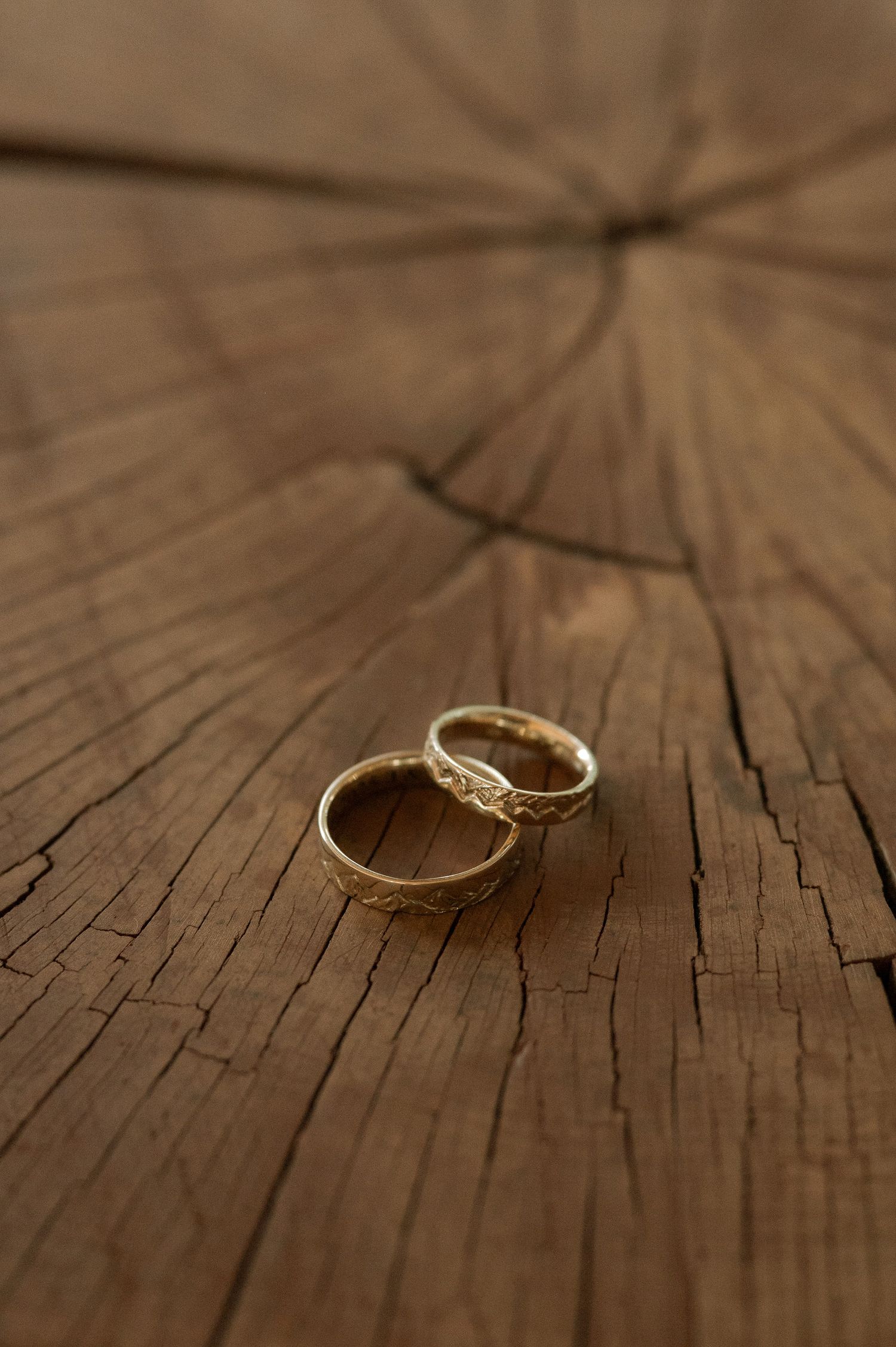 A gold ring with a small diamond sits on a rustic wooden surface with natural grain patterns and cracks.