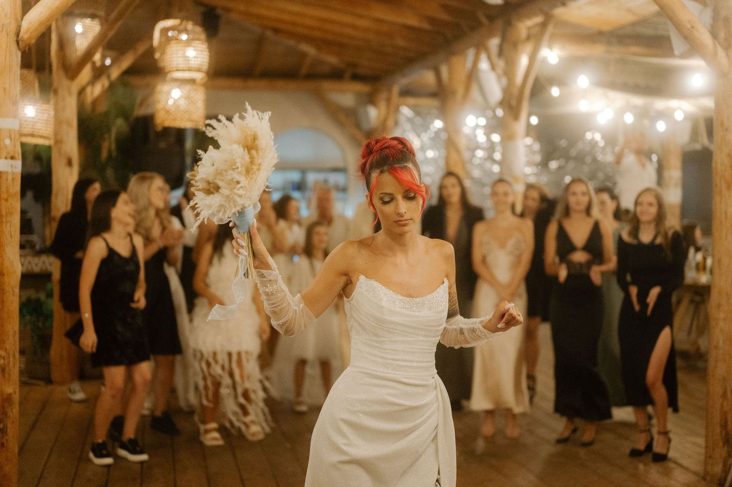 Wedding guests dance and celebrate under warm string lights in a rustic barn venue during a reception party.