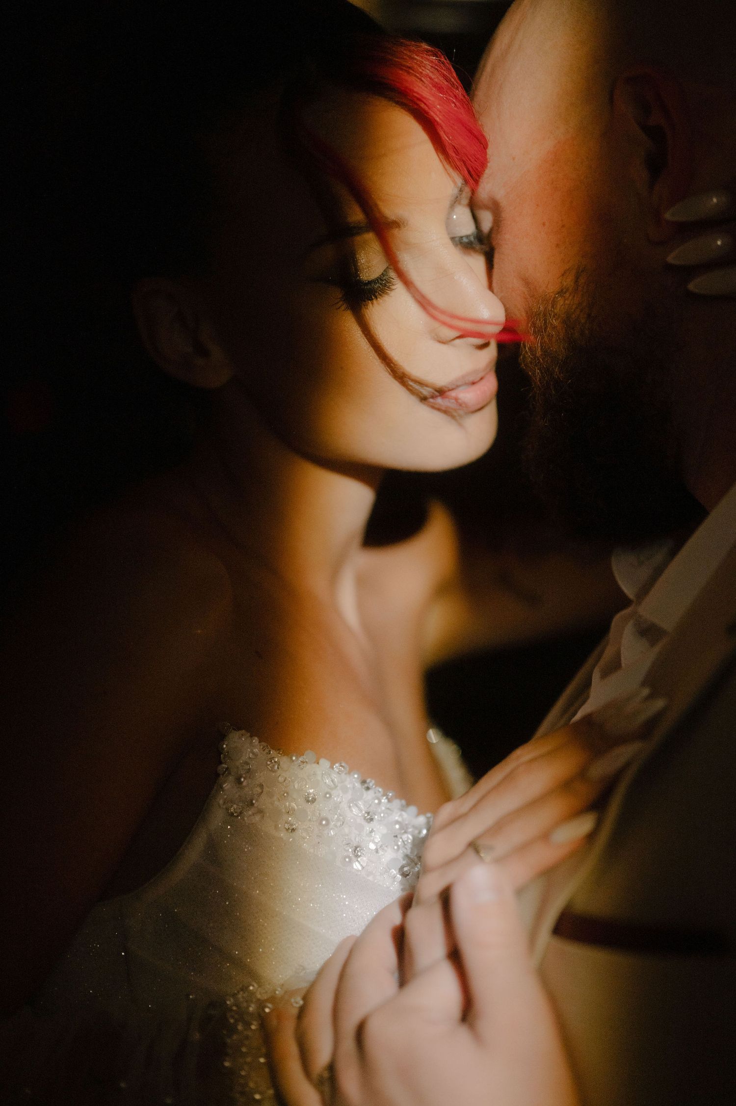 A romantic close-up of a bride in a white beaded dress with red lipstick in dramatic lighting.