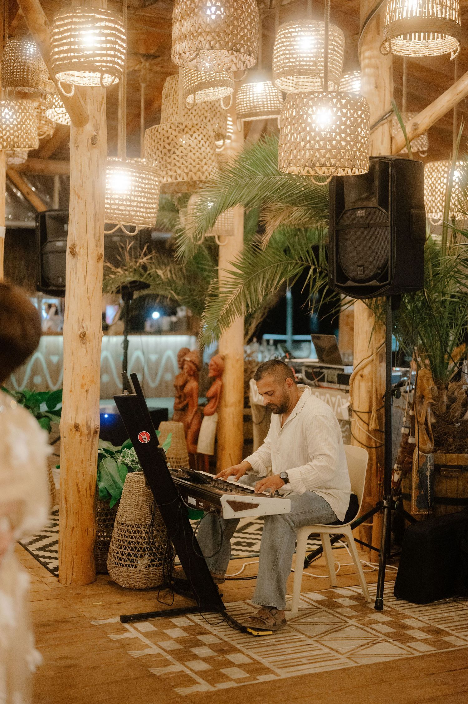Elegant restaurant interior with crystal chandeliers, white pillars, and palm plants creating a warm, luxurious ambiance.